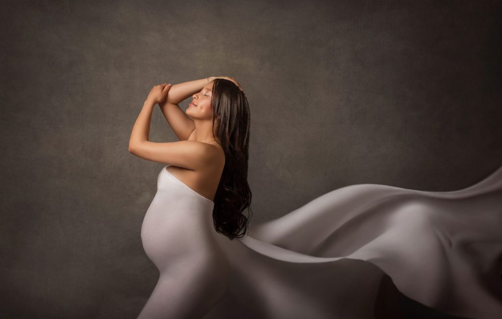 Mujer embarazada con un espectacular vestido blanco con cola larga posando en su sesión de maternidad